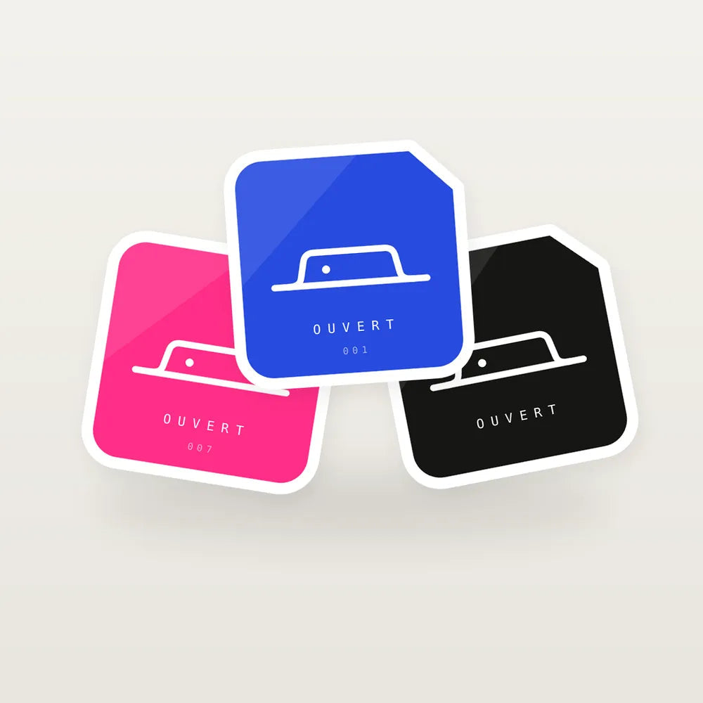 Trois stickers découpés en forme de sceau — bleu, rose et noir — avec liseré blanc